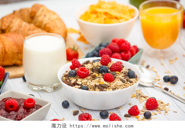 餐桌上丰盛的早餐早餐在早上享用，黄油羊角面包和玉米片全麦和葡萄干，牛奶在杯子里，草莓，蓝莓，覆盆子，猕猴桃，新鲜橙汁放在早餐桌上.